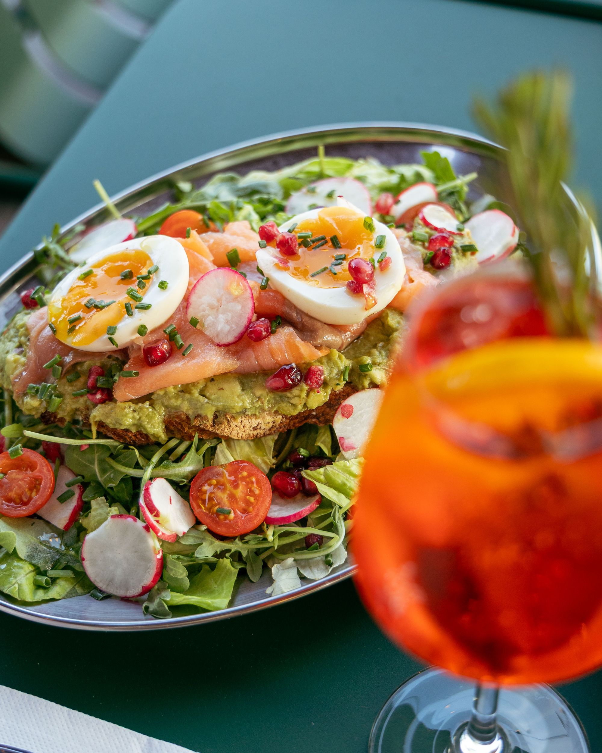 Avocado toast au saumon fumé, œufs mollets et grenade sur assiette métal, avec un spritz, chez Toto's à Rouen
