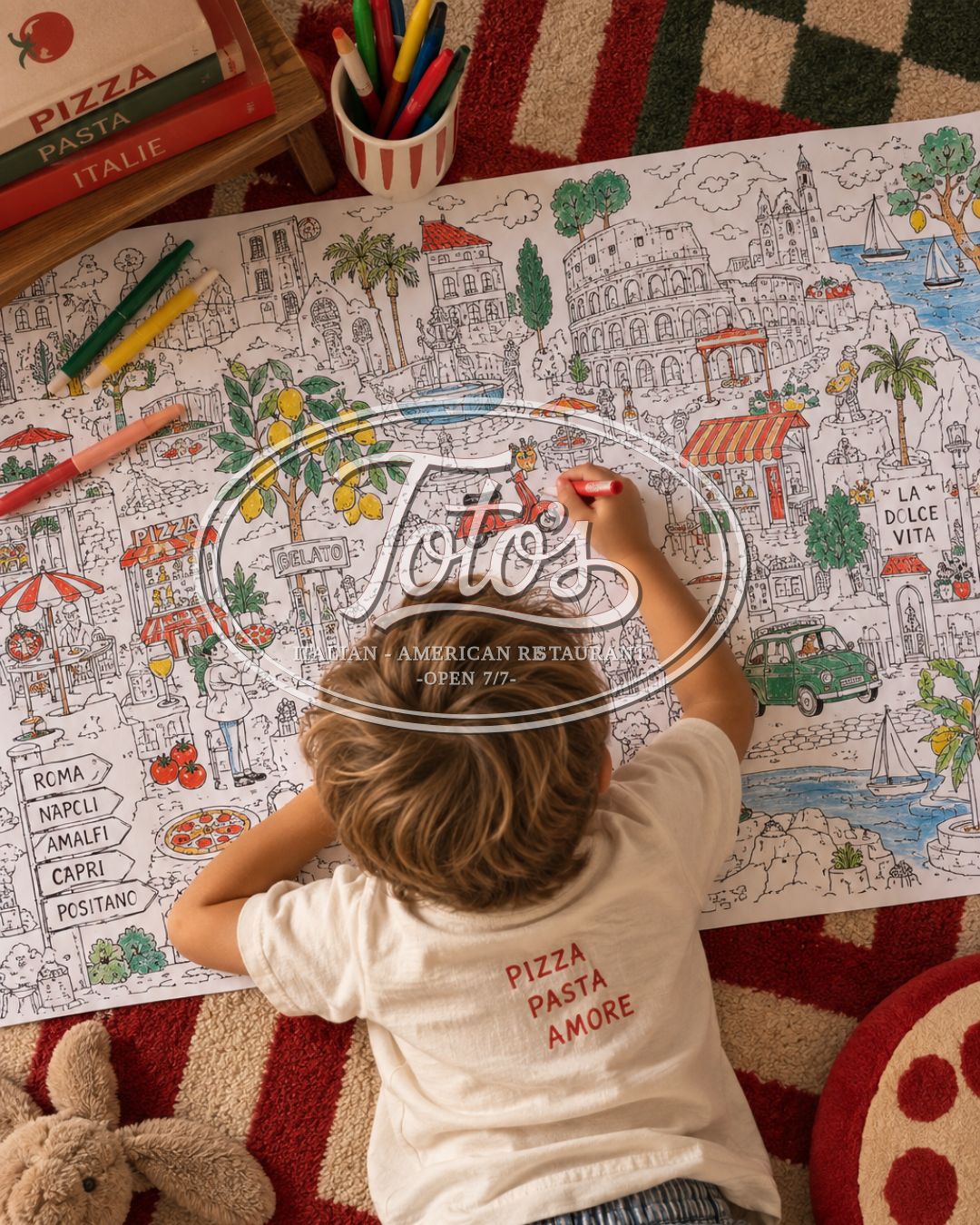 Un enfant allongé sur un tapis damier colorie une grande frise illustrant l'Italie, feutres et livres de cuisine autour de lui