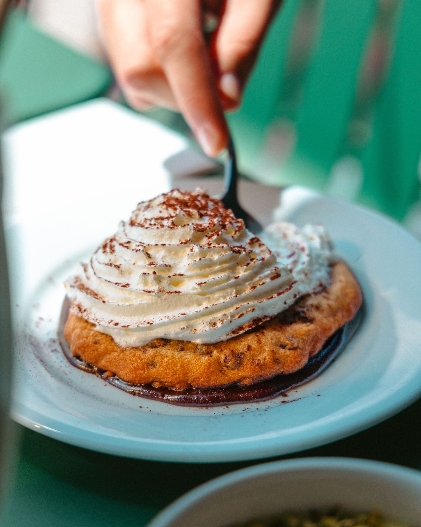 Cookie nappé de crème fouettée et de cacao, cuillère à la main, sur une table de Toto's